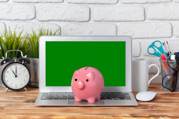 Piggy money box with laptop on wooden table