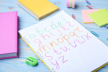Handwritten alphabet in notebook with stationery on blue wooden table