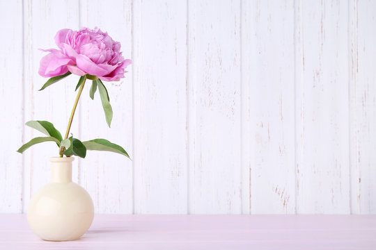 Bouquet of peony flowers in vase on pink wooden table