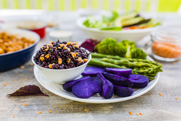 Delicious and healthy colorful vegetables with black rice and lentils on wooden table in the garden. Rainbow food and balanced food.