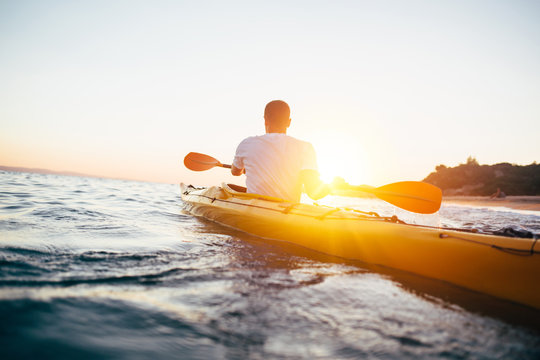 Man kayaker paddling kayak at sunset