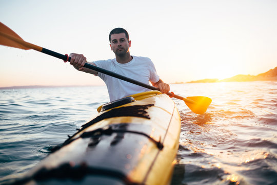 Man paddling kayak at sunset sea