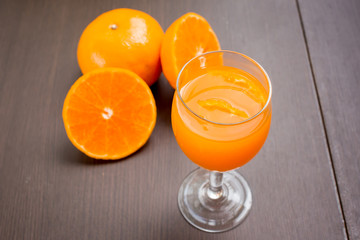 Glass of freshly pressed orange juice with sliced orange half on wooden table