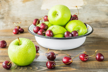 Fresh ripe cherries and green apples in white bowl on the kitchen table