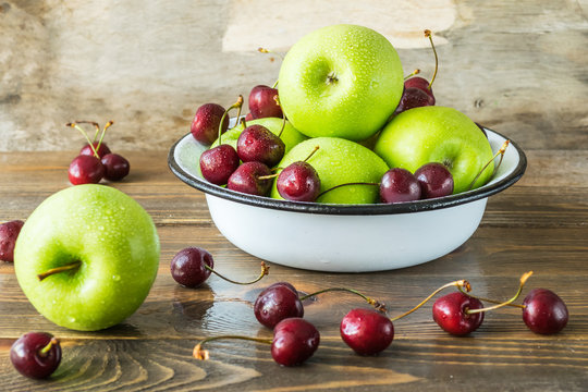 Fresh ripe cherries and green apples in white bowl on the kitchen table