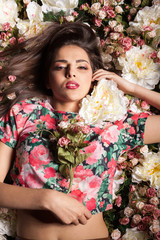 Attractive sensual woman lying on flowers in studio photo. Beauty and fashion. Cosmetics and skincare