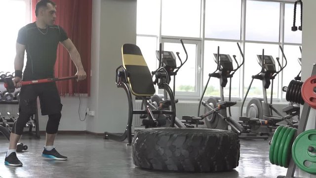 Male fitness model training workout witth heavy and big tire and hammer in fitness center