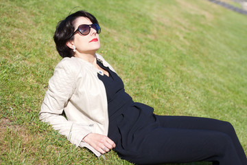 attractive latin woman with sunglasses turning her face toward the sun while relaxing on lawn