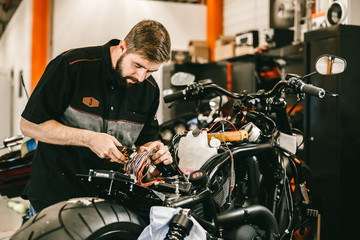 Fototapeta na wymiar Professional motorcycle mechanic works with electronics, cuts wires. Handsome mechanic working in bike repair shop.