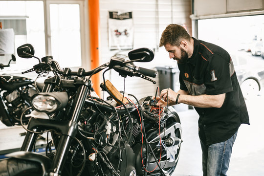 Professional motorcycle mechanic working in bike repair service. Mechanic checking a bike battery level with voltmeter in garage