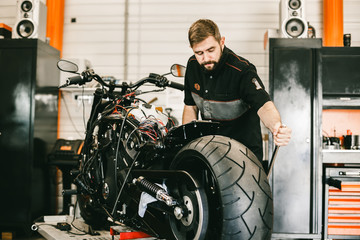 Mechanician changing motorcycle wheel in bike repair shop. Professional motorcycle mechanic working in bike repair service.