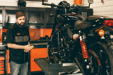 Professional moto mechanic raises a motorcycle on the lift. Man pressing up and down switch in bike repair shop.