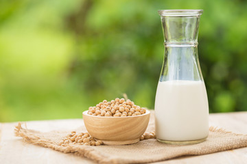 Soy milk and soy beans in wooden cup with abstract blurred forest nature background.