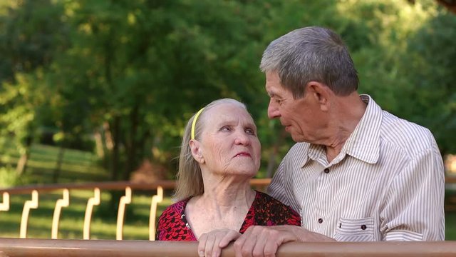 Portrait of elderly grandparents in the Park gazebo, slow motion. Grandma and grandpa look at each other with tenderness standing in a Park.