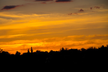 Fototapeta premium Orange sunset over silhouettes of village and trees