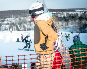 people in ski suit holding snowboards on a snowhill view from back