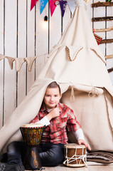 boy sitting on the floor and playing drum near wigwam in decorated wooden room © Ievgen Skrypko