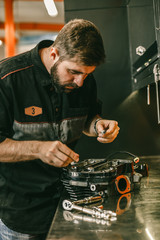 Motorcycle mechanic replacing glow plugs in bike engine. Spark plug replacement work in repair shop.