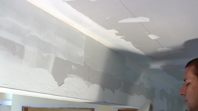 Homeowner puts joint compound over seam of drywall between wall and ceiling.