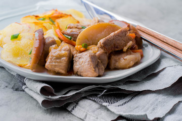 Pork stewed with apples with potatoes for garnish on plate on gray table background.