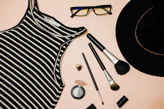 Hipster style. Ladies fashion accessories. Eye shadow, blush, red lipstick, makeup brushes, glasses, t-shirt striped on a pink background. Summer collection.