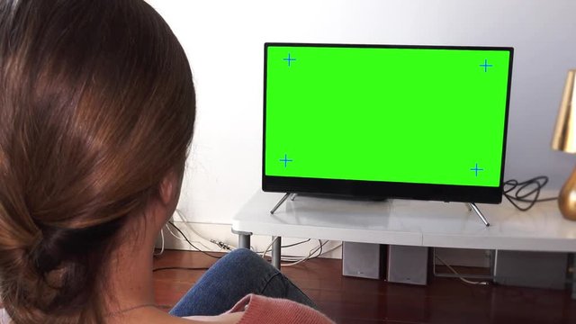 Girl In Living Room Zoom Out From Green Screen Tv. Young woman watching television zoom out from green screen. Shot behind models shoulders