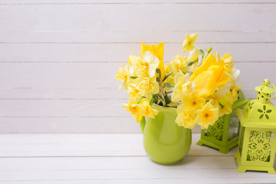 Bright yellow spring daffodils or narcissus flowers in green  pitcher and decorative green lanterns
