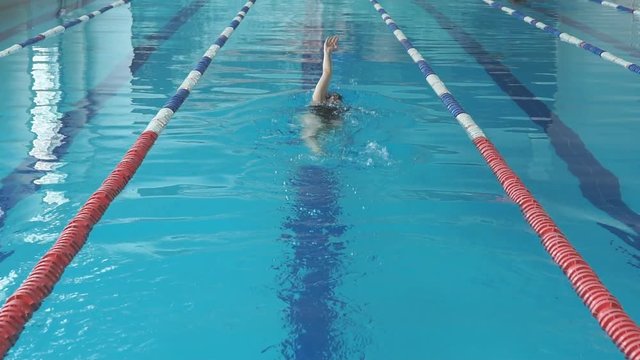 Young girl in goggles and cap swimming back crawl stroke style in the blue water pool