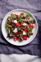 Plate of strawberry salad with balsamic vinegar, fennel, cream cheese, walnuts and greens on gray linen napkin. Easy summer food concept.