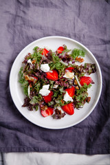Plate of strawberry salad with balsamic vinegar, fennel, cream cheese, walnuts and greens on gray linen napkin. Easy summer food concept.