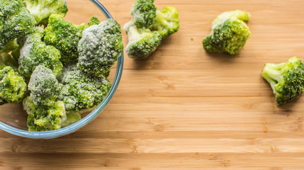 Frosen broccoli in a glass bowl on a wooden surface