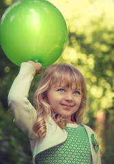 Portrait of a beautiful little blonde girl with green balloon in the park at the sunny summer day.