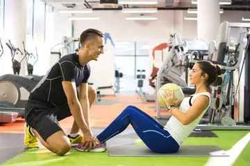 Tuinposter Female client doing abdominal crunches with ball while her personal trainer assisting her. © Bojan