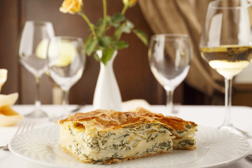 Cheese and spinach pie arranged on a plate, Wineglass in the background, Traditional dish in elegant setting, Selective focus with soft light