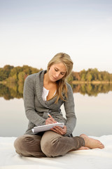Fototapeta na wymiar Young woman writing,sketching, by lake