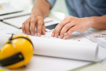 Hands of engineer working with the tool on project drawings background at construction site