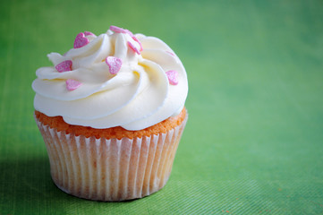 Cupcake with whipped cream and pink confectionery sprinkling In the form of hearts on green background. Picture for a menu or a confectionery catalog.