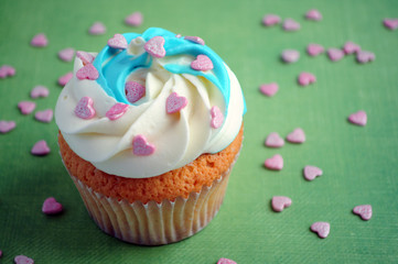 Cupcake with whipped cream and pink confectionery sprinkling In the form of hearts on green background. Picture for a menu or a confectionery catalog.