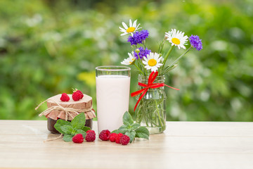 Glass of raspberry yogurt  with fresh berries of raspberry. Chamomile with cornflowers in vase on the table