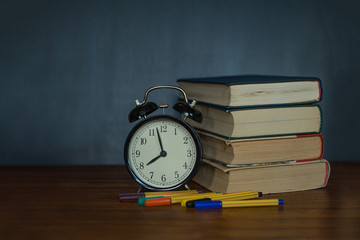 Books and an alarm clock stand on the background of a school board