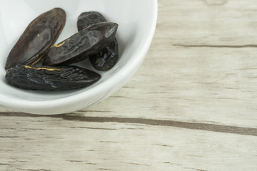 Tonkabohnen in weißer Porzellanschale, angeschnitten im linken oberen Bildrand, Holzhintergrund, Textfreiraum