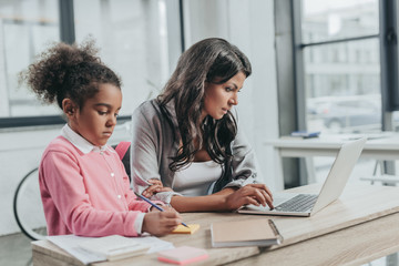 focused businesswoman working on laptop while daughter drawing on sticker