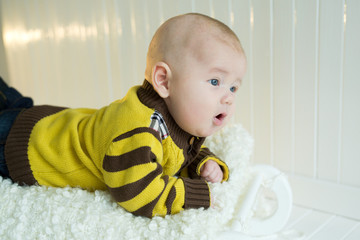 Portrait of a beautiful little boy in a bright yellow suit lying on his stomach with an amazed face