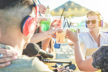 Group of friends cheering with tropical cocktails at video feed from beach kiosk party - Young...