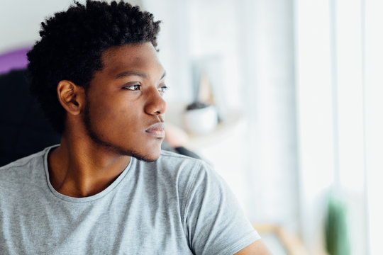 Melancholic headshot portrait of young black man looking aside isolated on blurred indoors background.