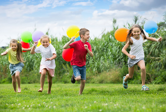 Four Cheerful Kids Running On Green Lawn