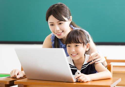 Young Teacher Helping Child With Computer Lesson