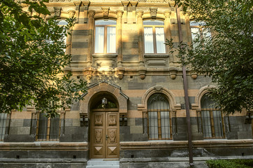 Old building of multicolored tufa stone with carved arches,columns and cornices surrounded by trees