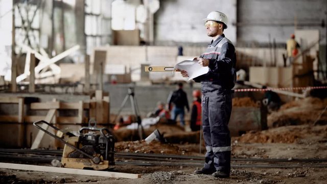 Male worker on site. Side view of man in uniform standing with project plan in hands on background of site.