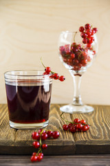 Cool summer currant juice in a glass next to fresh red currant